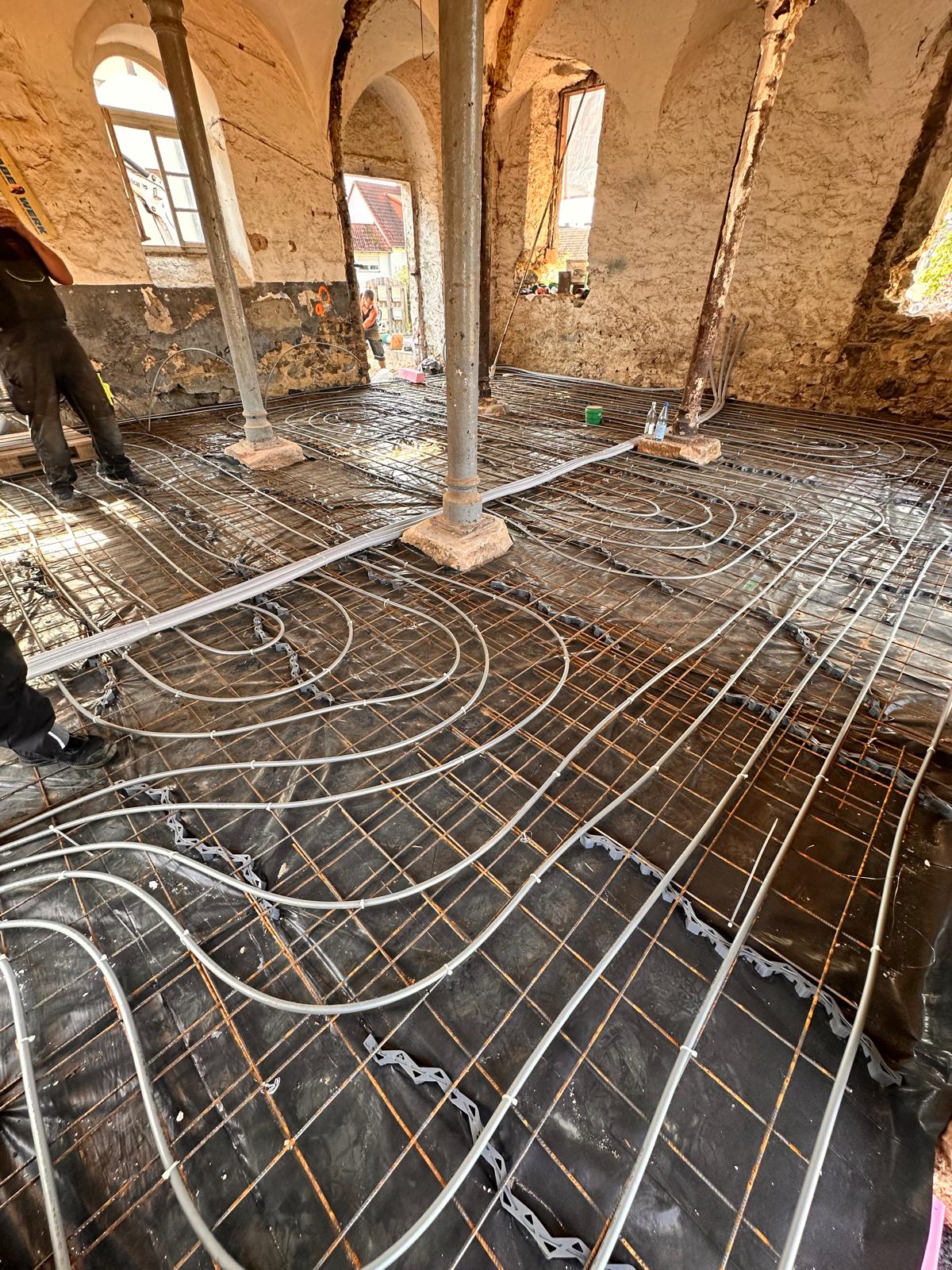 Verlegte Rohre der Betonkernaktivierung zwischen Gusseisensäulen in einem alten Gewölberaum