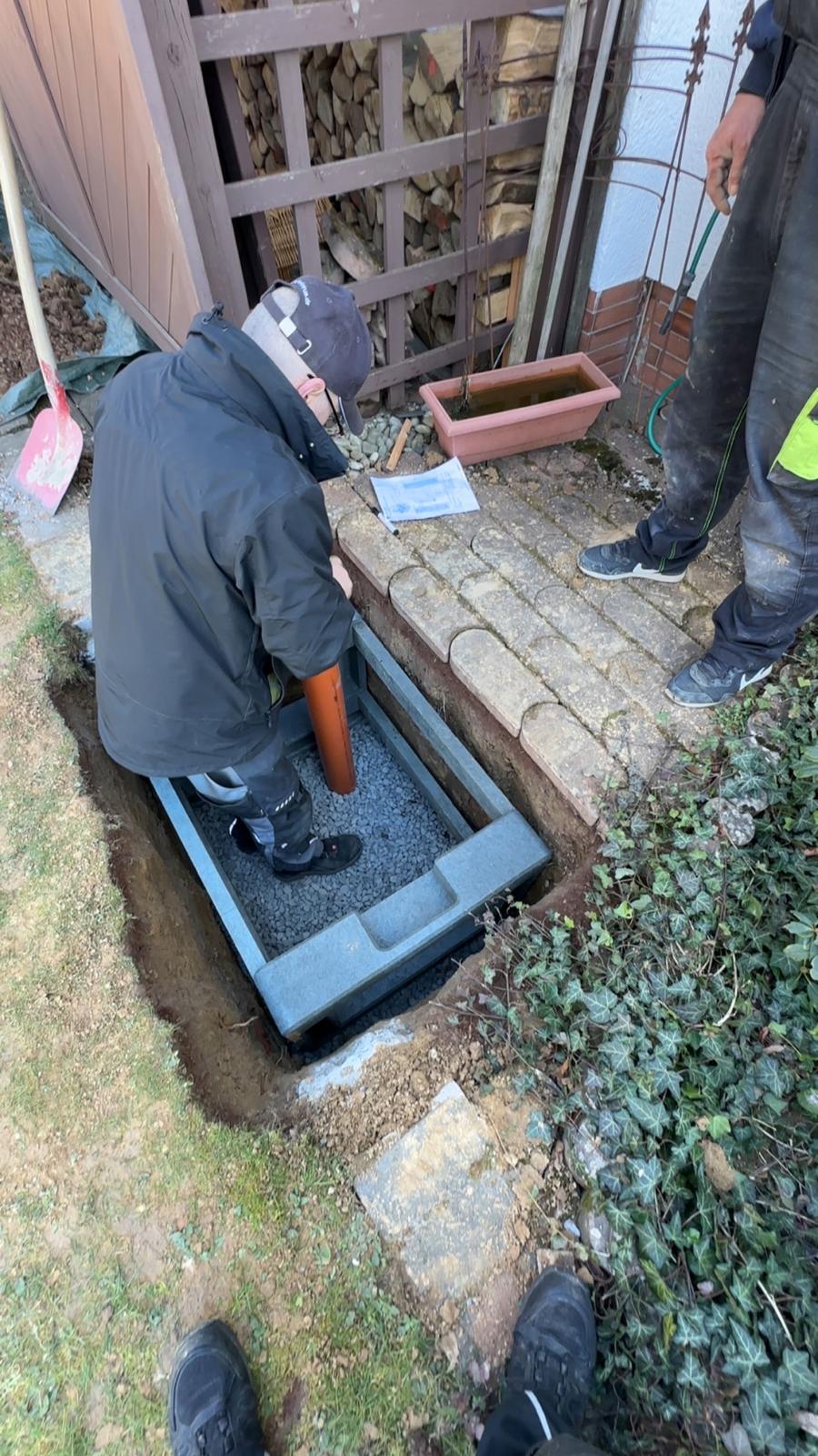 Mitarbeiter setzt das Fundament für eine Wärmepumpe mit Kiesbett und Kondensatrohr